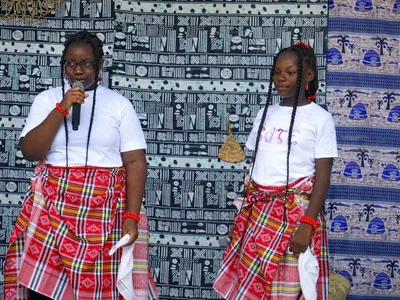 Two BRIF students in traditional dress speak to an audience during a cultural day celebration.