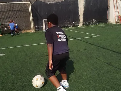 A BRIF student takes a shot during a football training session on the school's pitch, wearing a British & French Academy kit.